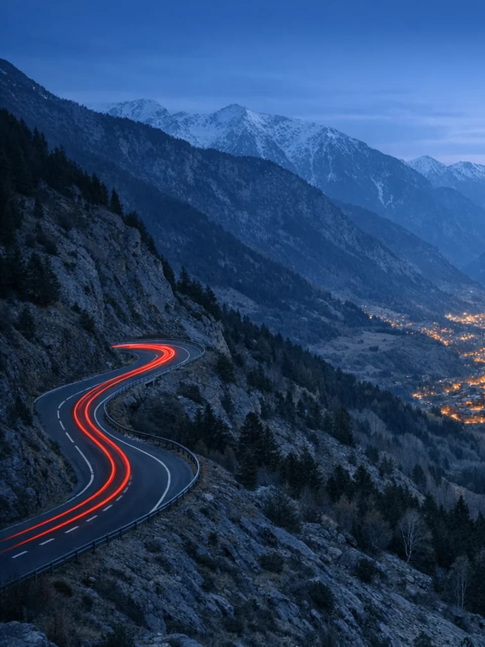 Dusk view across the Andorra valley with a winding mountain road and town lights below.